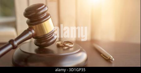 Un giudice di legno gavel su un tavolo accanto a due fedi nuziali e una penna, simboleggiando le questioni legali relative al matrimonio o al divorzio Foto Stock