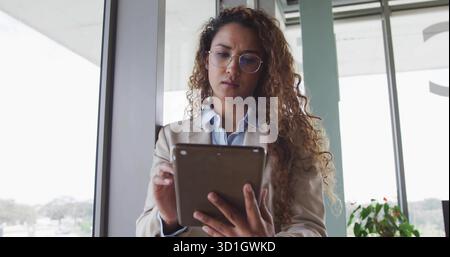 Con un tablet, un blazer professionale che analizza i dati in un ufficio moderno, con vista sullo skyline della città Foto Stock