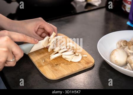 Primo piano di funghi champignon tagliati su un tagliere di legno, pronti per la cottura in una cucina casalinga. Foto Stock