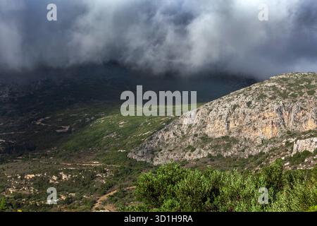 Basse nuvole di tempesta si riversano sulle verdi colline e le aspre scogliere dell'isola di Citera, in Grecia, con luce solare e ombra che spazia la valle. Foto Stock