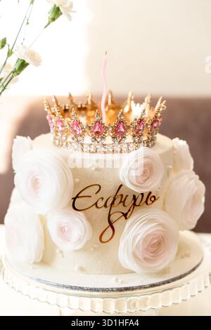 Una torta splendidamente decorata adornata con rose bianche e una corona dorata, che crea un centro lussuoso ed elegante. Foto Stock