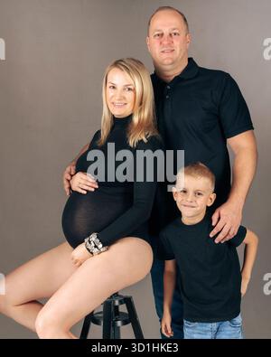 Donna incinta seduta con marito e figlio in studio accogliente maternità ritratto di famiglia che simboleggia la felicità e l'attesa Foto Stock