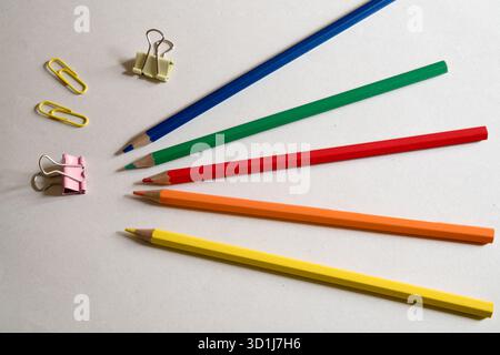 Una vivace disposizione di matite colorate, graffette metalliche e clip leganti, pronte per lo studio o il lavoro creativo. Foto Stock