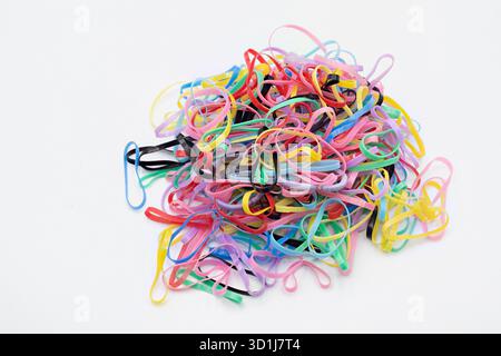 Molti cravatte elastiche colorate per capelli, che formano un cumulo casual su uno sfondo bianco. Rappresenta connessione, organizzazione e accessori quotidiani Foto Stock