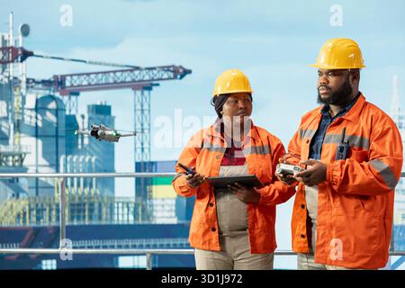 Team di progettazione su piattaforma offshore che esegue indagini sul sito utilizzando un sistema di droni automatizzato. I colleghi di lavoro di squadra utilizzano la tecnologia della fotografia aerea per determinare le posizioni ottimali per i pattini di perforazione Foto Stock