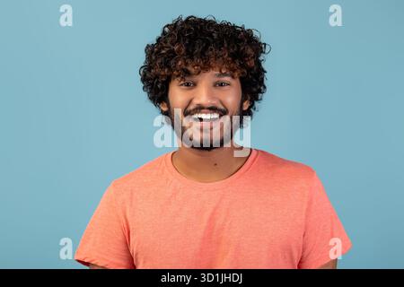 Bel giovane con capelli ricci e barba su sfondo blu con camicia rosa Foto Stock