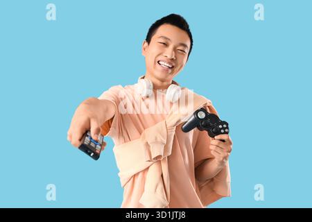 Giovane asiatico con telecomando TV e gamepad su sfondo blu Foto Stock