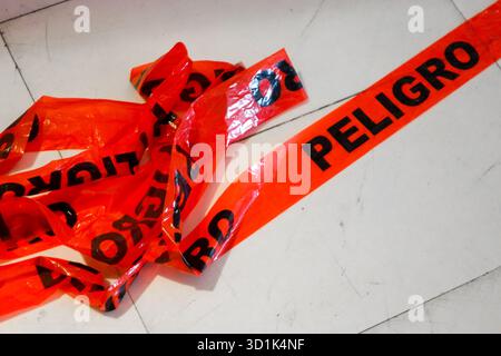 Nastro segnaletico rosso brillante con la parola "Peligro" in spagnolo adagiata su un pavimento piastrellato bianco che indica un'area pericolosa o limitata Foto Stock