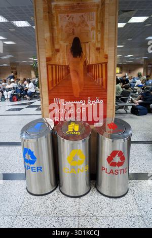 Contenitori per il riciclaggio di carta, lattine e plastica in un terminal aeroportuale egiziano con un poster turistico della Tomba di Ramses sullo sfondo Foto Stock