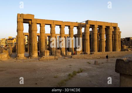 Antiche colonne in pietra del Tempio di Luxor illuminate dalla calda luce del sole in Egitto con persone che camminano per il sito archeologico, l'Egitto Foto Stock