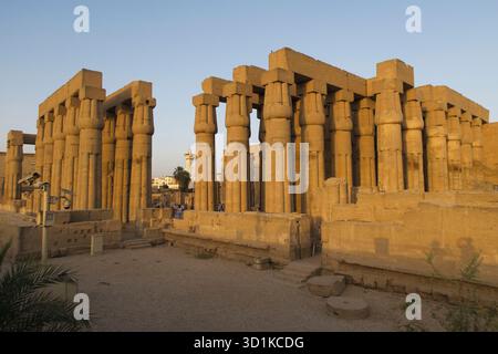 Antiche colonne in pietra del Tempio di Luxor illuminate dalla calda luce del sole in Egitto con persone che camminano per il sito archeologico, l'Egitto Foto Stock