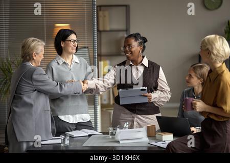 Donna caucasica di mezza età che stringe la mano con donna nera di mezza età in ufficio Foto Stock