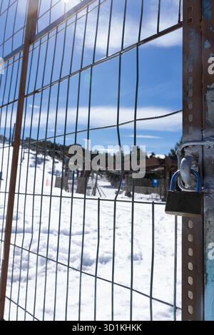 Recinzione in filo metallico e lucchetto chiudono una stazione sciistica durante la bassa stagione, con neve a terra Foto Stock