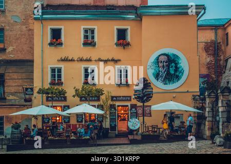 L'immagine mostra un'affascinante scena di strada con un edificio dai colori vivaci che ha un ristorante o caffetteria al piano terra. Ci sono diversi tavoli Foto Stock