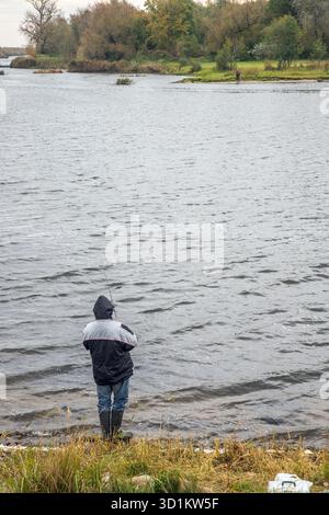 Un uomo che pesca a Rusne, sul lato di skirvyte rive, Lituania. Dall'altra parte (Kaliningrad Russia lato) di fiume un altro uomo pesca Foto Stock
