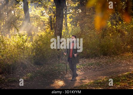L'uomo cammina lungo un sentiero illuminato dal sole in una foresta autunnale, circondato da un fogliame vivace e da una luce soffusa che filtra tra tra gli alberi Foto Stock