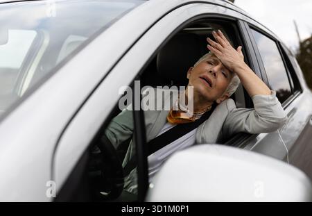 Donna d'affari matura e stressata seduta sul sedile del conducente di un'auto che si palma mentre è bloccata in un ingorgo stradale Foto Stock