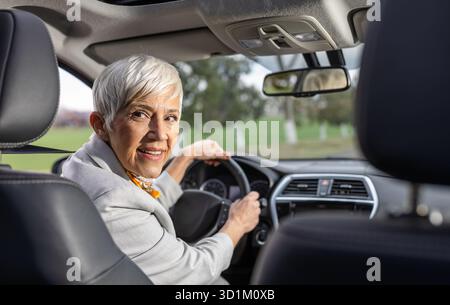 Donna anziana sorridente seduta in macchina e che guarda indietro sul sedile Foto Stock