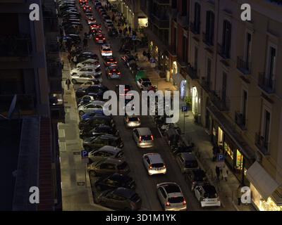 Vista dall'alto di una vivace strada urbana al crepuscolo. Una linea lenta di auto con luci di arresto accese si sposta tra veicoli ad alta densità di parcheggio su entrambi i lati. SCO Foto Stock