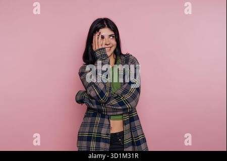 Donna sorridente con camicia a quadri che copre il viso su sfondo rosa. Foto Stock