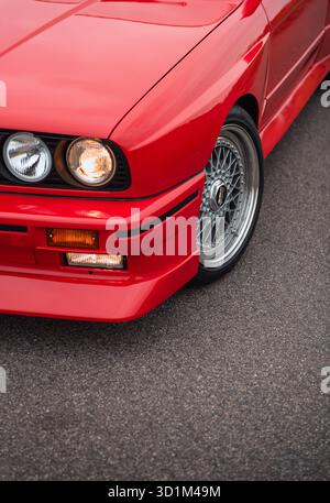 Vista dell'angolo anteriore sinistro della BMW M3 E30. Primo piano di un'auto sportiva rossa brillante degli anni '1980 su strada asfaltata. Foto Stock