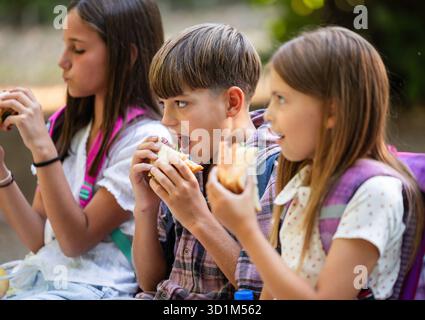 Primo piano di tre amici delle scuole medie che mangiano panini all'aperto per la pausa pranzo Foto Stock