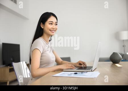 Donna asiatica sorridente che lavora a distanza da casa Foto Stock