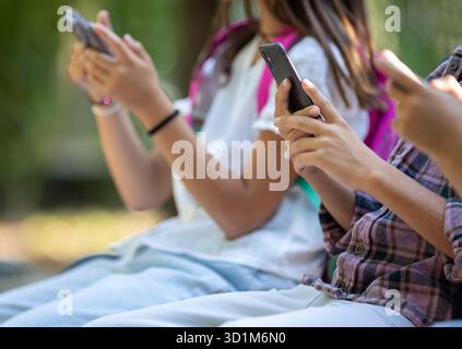 Tre bambini seduti su una panchina scolastica a giocare ai videogiochi. Immagine ravvicinata di un ragazzo che tiene in mano uno smartphone con entrambe le mani. Foto Stock