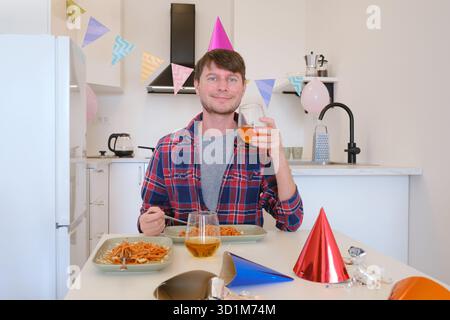 Il giovane festeggia il suo compleanno a casa, circondato da un ambiente accogliente e festoso. Ama la sua giornata speciale con bevande, pasta e vino per festeggiare, gustare pasti e applausi Foto Stock
