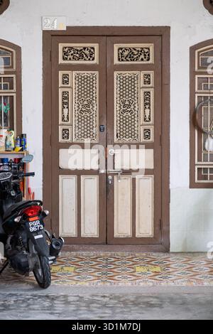 Una porta in legno splendidamente lavorata con motivi dettagliati spicca in evidenza, accompagnata da una motocicletta parcheggiata su un pavimento a motivi geometrici. Foto Stock