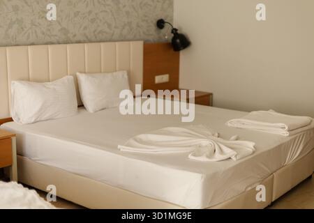 Una comoda camera da letto presenta un letto ben fatto con lenzuola bianche e morbidi cuscini. L'illuminazione calda e l'arredamento semplice creano uno spazio rilassante per rilassarsi Foto Stock