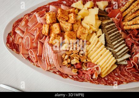 Primo piano di un piatto di salumi con affettati assortiti, cubetti di formaggio, noci e cracker su un piatto bianco. Foto Stock