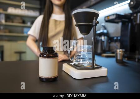 Primo piano di una bottiglia di plastica e di una macchina per il caffè con funzione "pour-over", messi sul bancone e un addetto al bar Foto Stock