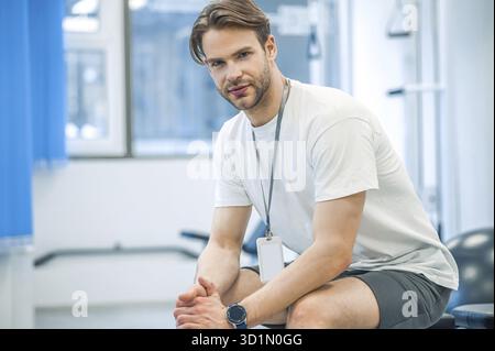 In una palestra. Giovane uomo in abbigliamento sportivo seduto su un dispositivo di allenamento in palestra Foto Stock
