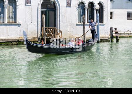 Venezia, Veneto - Italia - 06-10-2021: Gondoliere guida i turisti attraverso le tranquille acque dei canali di Venezia, lungo le mura storiche Foto Stock