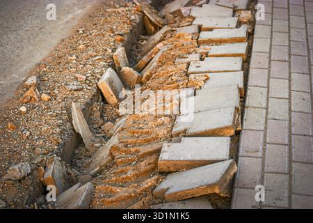 Costruzione di mucchi di sabbia, pietre adagiate sul marciapiede vicino ai pozzi per l'installazione tra la carreggiata e il sentiero. Asfalto e asfaltatori rotti Foto Stock