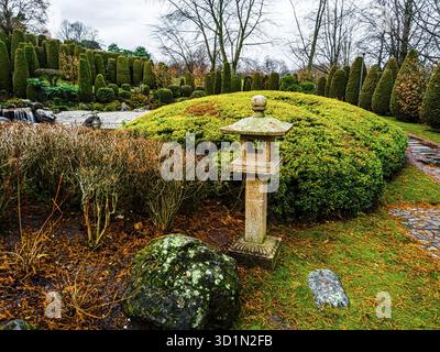 Vista di una tradizionale lanterna in pietra ishi-doro o ikekomi-doro circondata da massi decorativi e cespugli in un giardino giapponese a Bonn, Germania Foto Stock