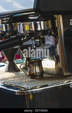 Primo piano del caffè erogato dalla macchina all'interno di un piccolo recipiente cromato. Produzione professionale di caffè nelle piccole aziende locali Foto Stock