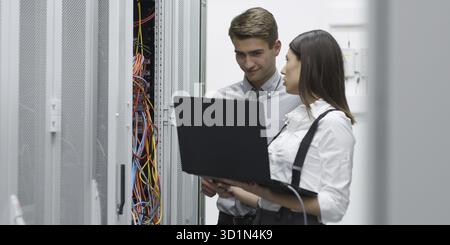 Tecnici che utilizzano computer portatile mentre il server di analisi in sala server Foto Stock