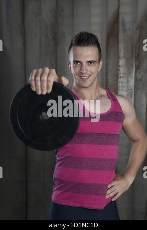 Uomo muscolare facendo esercizio con pesi nella palestra crossfit contro sfondo rustico Foto Stock