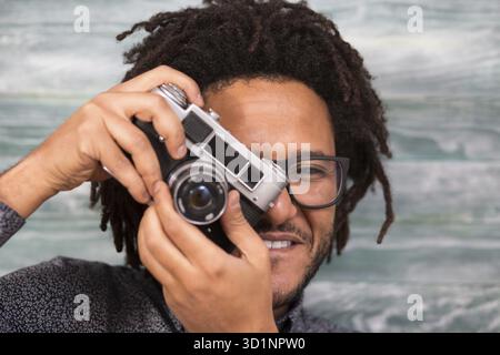 Felice hipster uomo sorridente con fotocamera giocattolo su rustiche backgorund Foto Stock