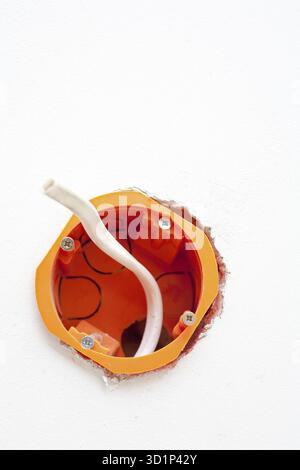 Cavo elettrico nella scatola arancione per l'installazione nel foro della parete intonacata, spazio imbottito, messa a fuoco selettiva Foto Stock