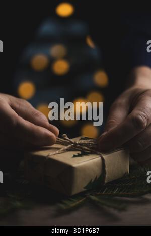 Primo piano delle mani di un uomo che lega un arco di iuta a un regalo di Natale. Rivestimento in stile ecologico con materiali naturali e calda atmosfera di vacanza. Imag perfetto Foto Stock