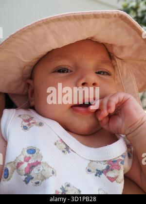 Il bambino indossa un cappello da sole seduto con la madre all'aperto, sorridendo alla luce naturale del sole. Connessione familiare e felicità d'infanzia. Foto Stock