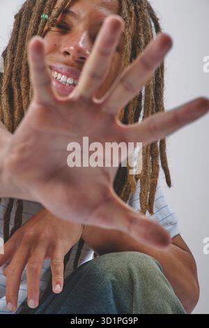 Persona gioiosa con dreadlock che si avvicinano con la mano in avanti guardando direttamente lo spettatore Foto Stock