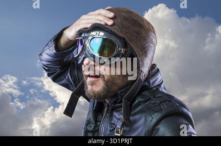 Il vecchio piano pilota su sfondo di nuvole temporalesche con viso espressivo. bicchieri e vecchio cappello nero con giacca di pelle Foto Stock