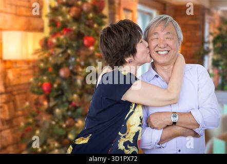 Felice coppia di anziani cinesi che si baciano davanti all'albero di Natale decorato. Foto Stock