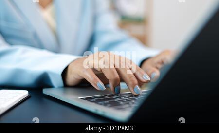 Primo piano di una donna che digita le mani sulla tastiera del notebook in un ufficio moderno. Concetto di lavoro da donna d'affari, comunicazione online e produttività digitale. Foto Stock