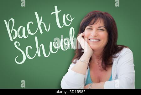 Back to School scritto su Green Chalkboard dietro la sorridente donna di mezza età Foto Stock