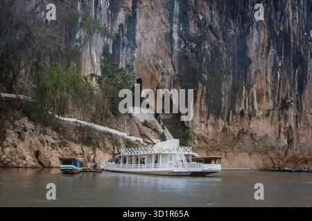 Luang Prabang, Laos - 10 marzo 2025: Nave da crociera turistica ormeggiata al fiume Mekong di fronte all'ingresso delle grotte buddiste Pak Ou. Foto Stock